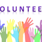A sign saying VOLUNTEER and showing raised hands in rainbow colors.
